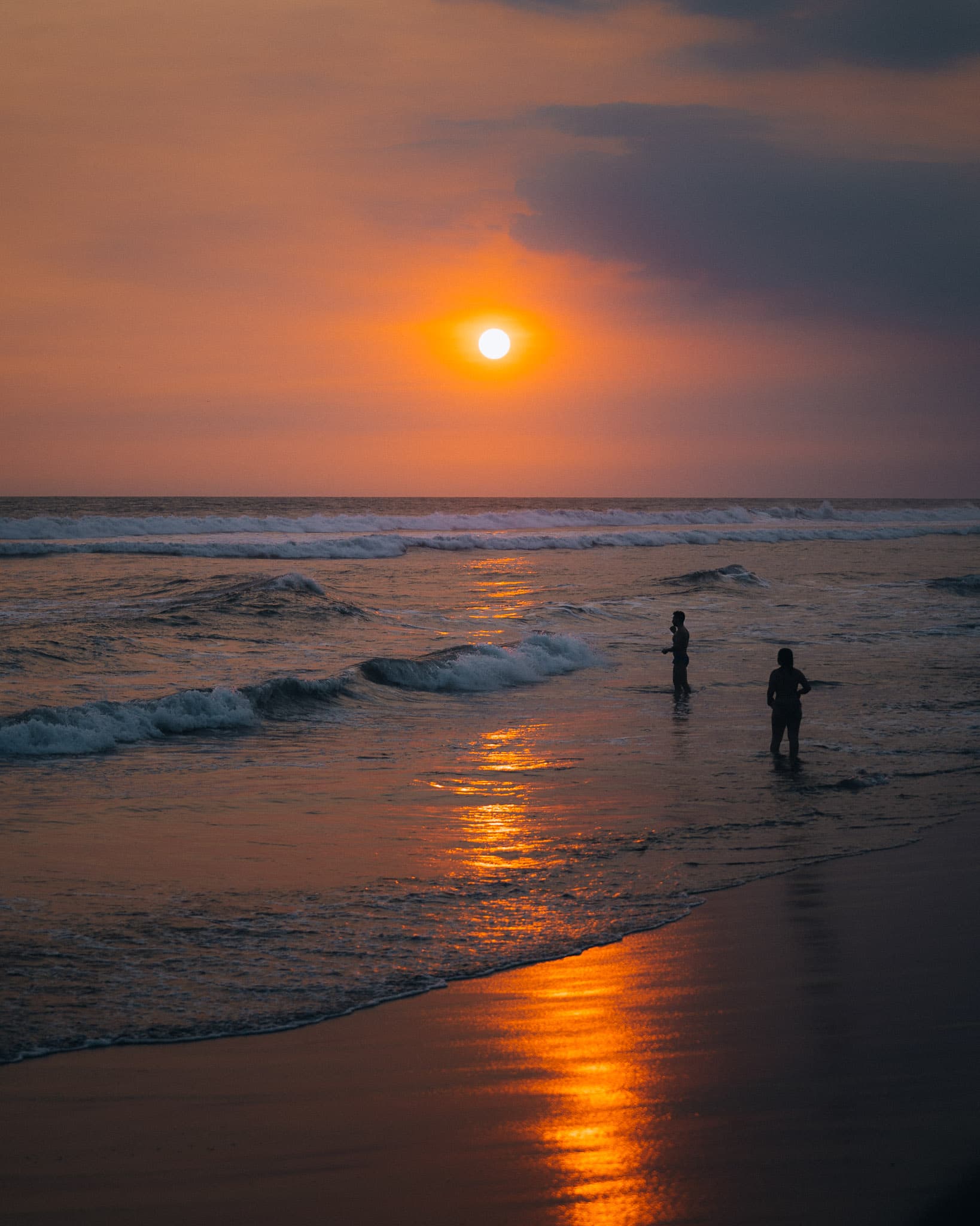 Two silhouettes standing in the surf at sunset on the Pacific coast