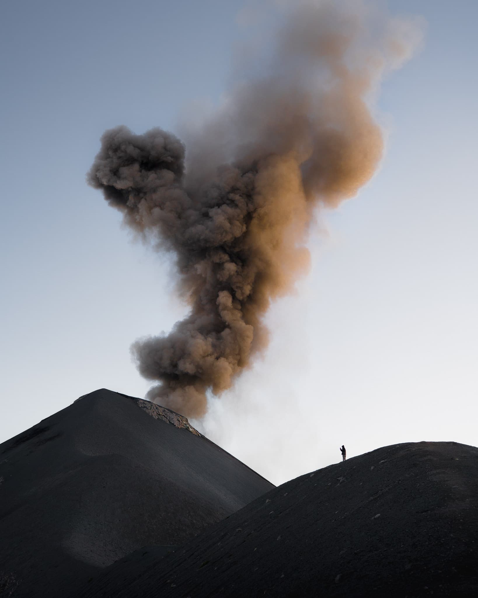 A lone figure silhouetted on the ridge of Acatenango as Volcán de Fuego erupts